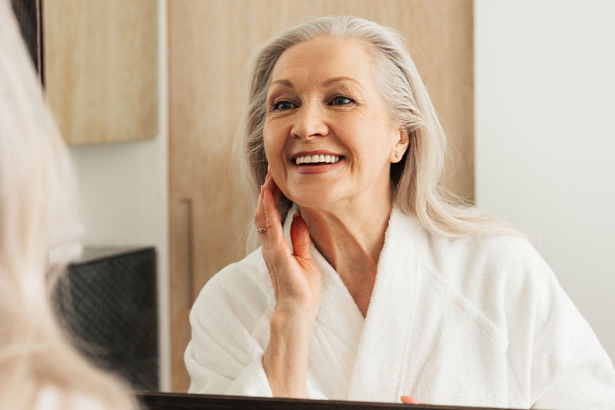 a woman looks in the mirror and smiles after getting a deep plane facelift in Daytona Beach, FL